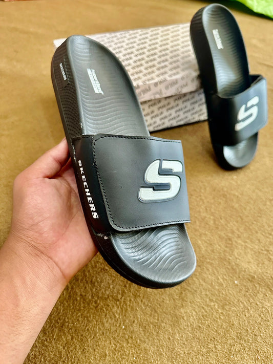 Black indoor slide sandals with logo, textured sole, held in hand on brown surface