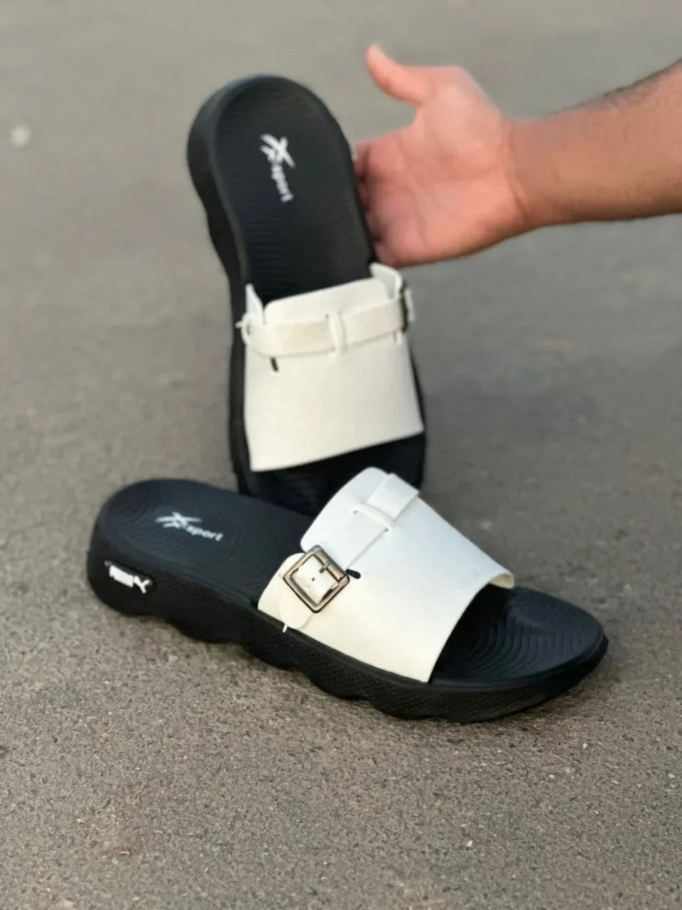 Black and white indoor sandals with buckles displayed on a textured surface